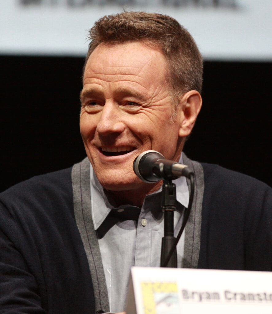 Bryan Cranston smiling at panel event wearing gray shirt and cardigan with microphone close-up Wallpaper