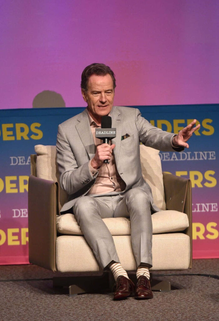 Bryan Cranston in light gray suit seated on modern chair at Deadline event vibrant gradient background Wallpaper