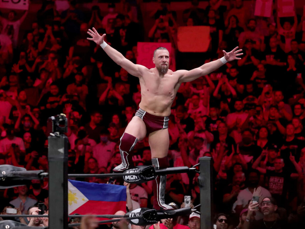 Bryan Danielson victorious pose on wrestling ropes with cheering fans and vivid red lighting wallpaper