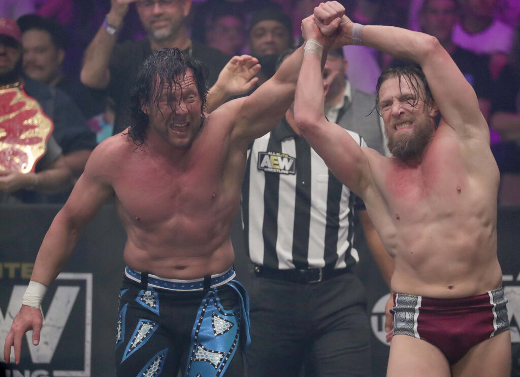 Bryan Danielson and Kenny Omega AEW wrestling match celebrating in ring with vibrant crowd lighting Wallpaper