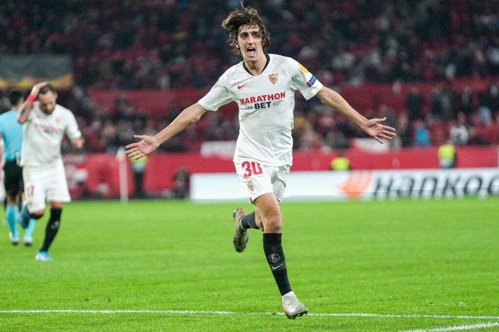 Bryan Gil celebrating wide open arms Sevilla FC white kit vibrant stadium high resolution action shot Wallpaper