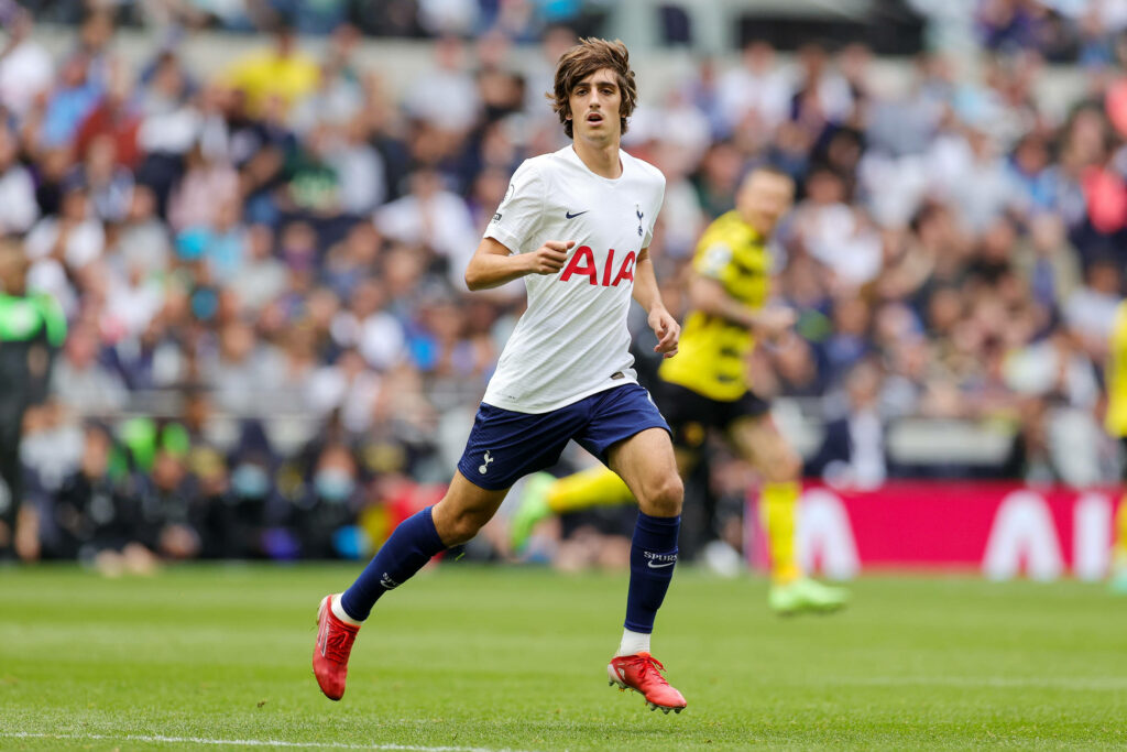 Bryan Gil sprinting on football stadium in white navy Tottenham Hotspur kit with vibrant crowd Wallpaper
