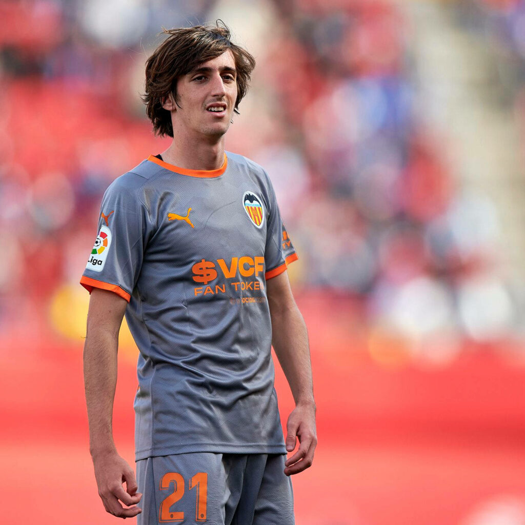 Bryan Gil in Valencia CF gray away jersey with orange accents on field stadium background wallpaper