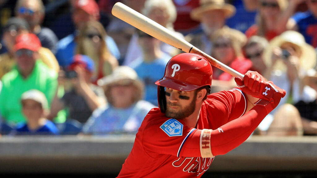Bryce Harper in red Phillies uniform batting at vibrant ballpark captures intense baseball moment Wallpaper