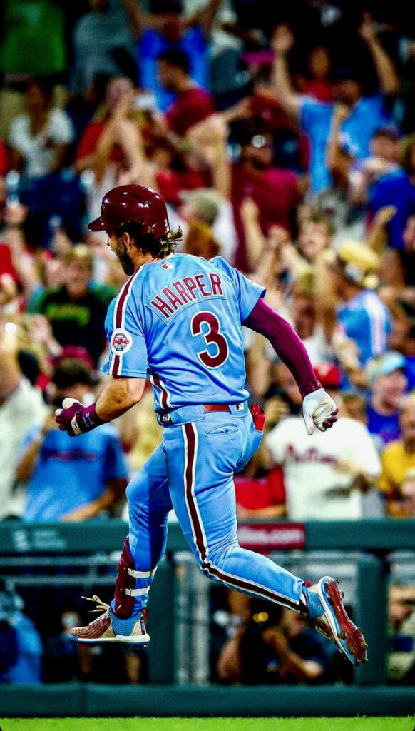 Bryce Harper jumping mid-air in powder blue Phillies uniform with cheering crowd background Wallpaper