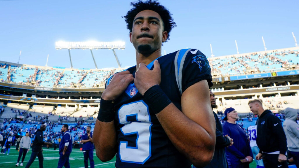 Bryce Young in Carolina Panthers jersey on football field under clear blue sky stadium backdrop wallpaper