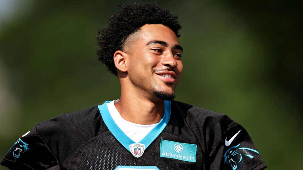 Bryce Young smiling in Carolina Panthers jersey outdoors vibrant sunlight green background wallpaper