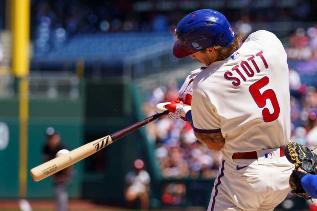 Bryson Stott mid-swing Philadelphia Phillies uniform dynamic baseball action vibrant stadium background Wallpaper