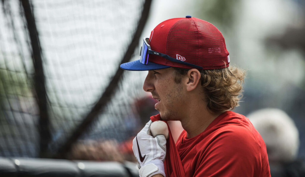 Bryson Stott in red jersey and cap focused during baseball game with blurred natural background Wallpaper