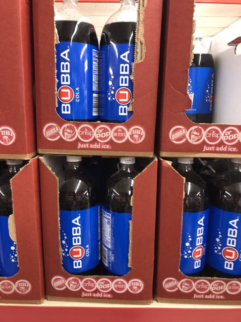 Bubba Cola bottles with blue labels in red display boxes on Save A Lot shelf under bright lights Wallpaper