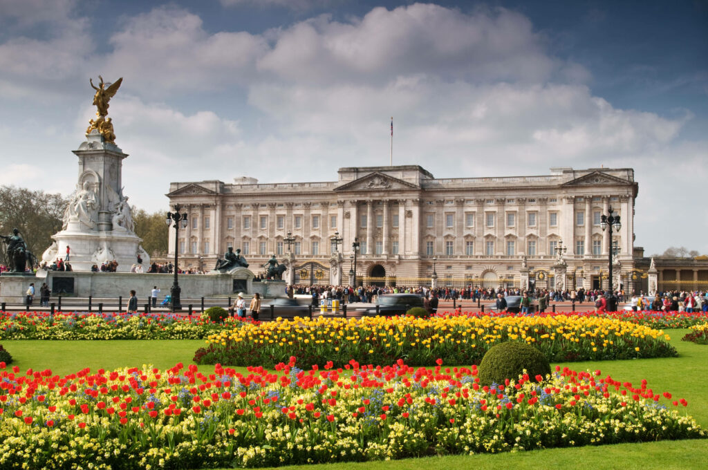 Buckingham Palace with vibrant tulips and lush garden under a bright partly cloudy sky wallpaper