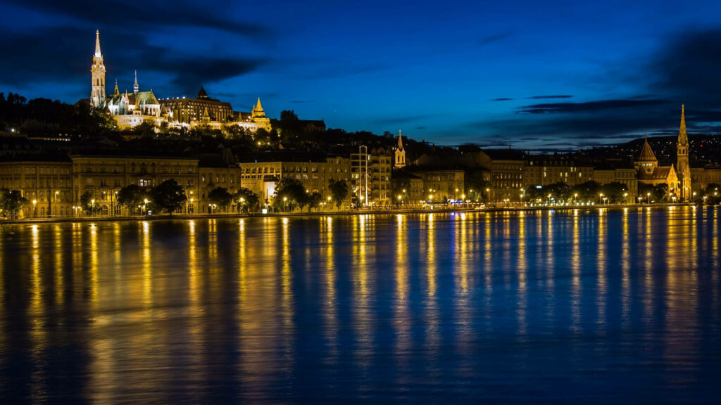 Budapest night cityscape with illuminated historic buildings reflecting on Danube River waters Wallpaper