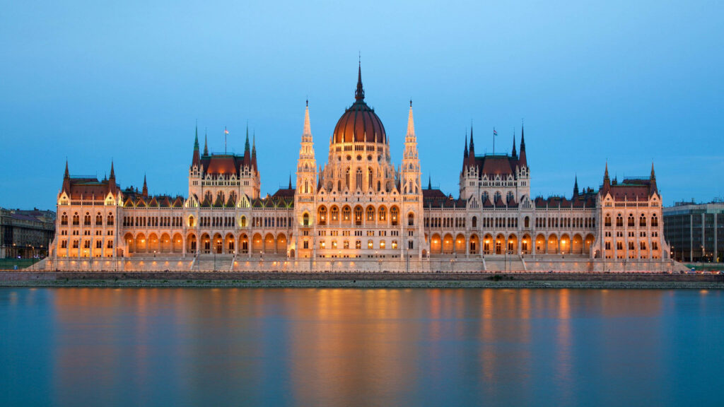 Budapest Parliament building illuminated at night reflected in calm water beautiful wallpaper background