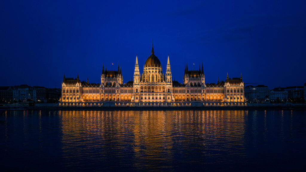 Budapest Parliament illuminated at night reflecting on Danube River under deep blue sky wallpaper background