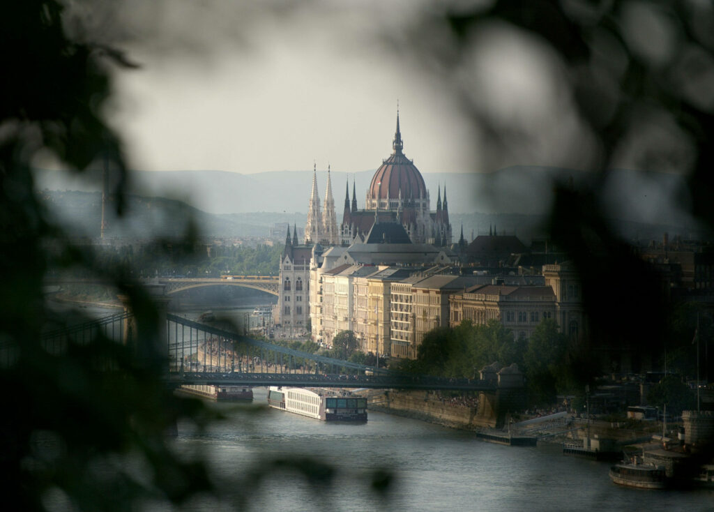 Budapest scenic wallpaper boat on river with iconic Parliament building framed by tree branches