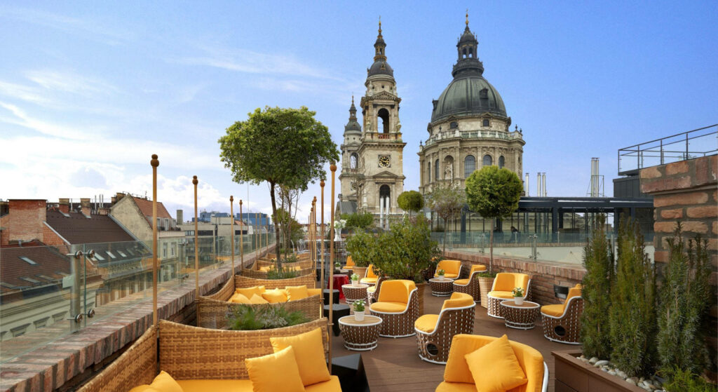 Rooftop lounge in Budapest with yellow chairs and St Stephens Basilica under clear blue sky Wallpaper