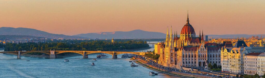Budapest skyline at sunset with Parliament building and boats on the Danube River wallpaper