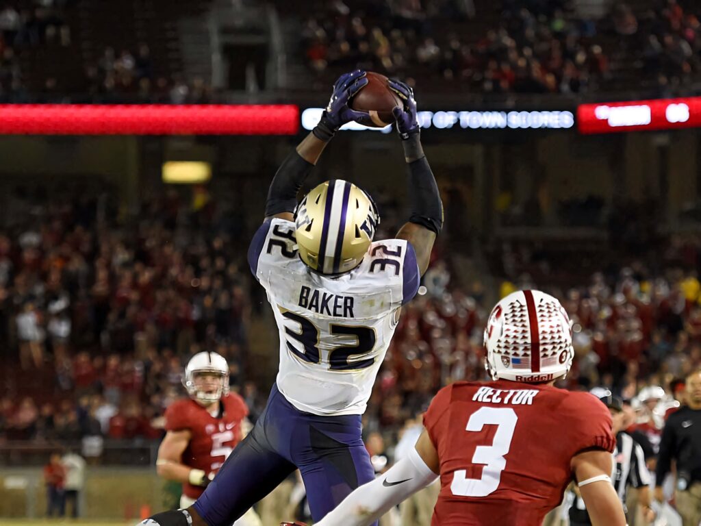 Budda Baker football catch leaping high under stadium lights vibrant team colors packed crowd Wallpaper