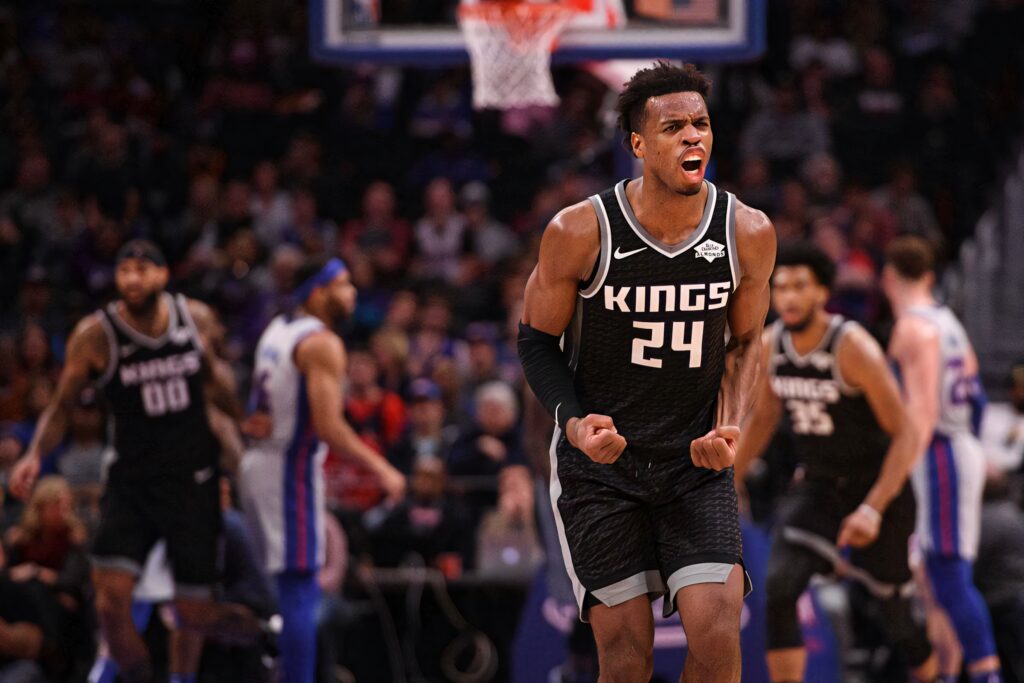 Buddy Hield mid-scream in Sacramento Kings jersey on basketball court with vibrant arena lights Wallpaper