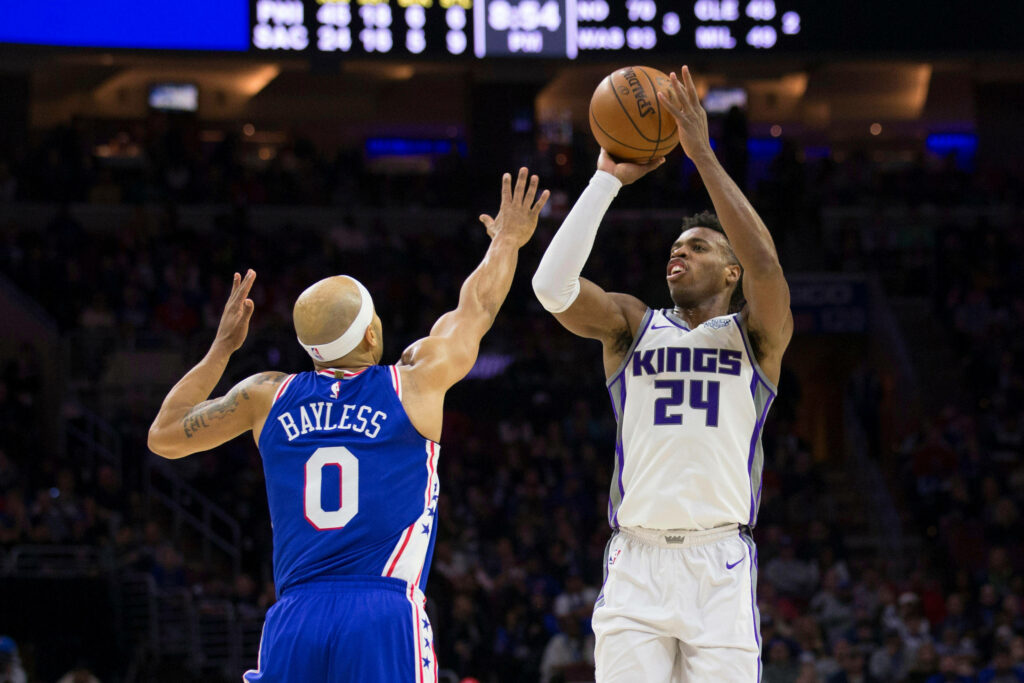 Buddy Hield Sacramento Kings mid-air three-point shot over defender vibrant game action basketball Wallpaper