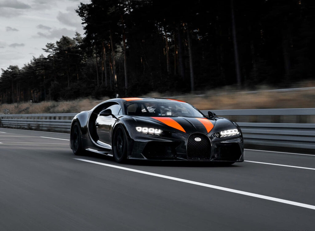 Bugatti speeding on open road with sleek black body and vibrant orange accents luxury car wallpaper