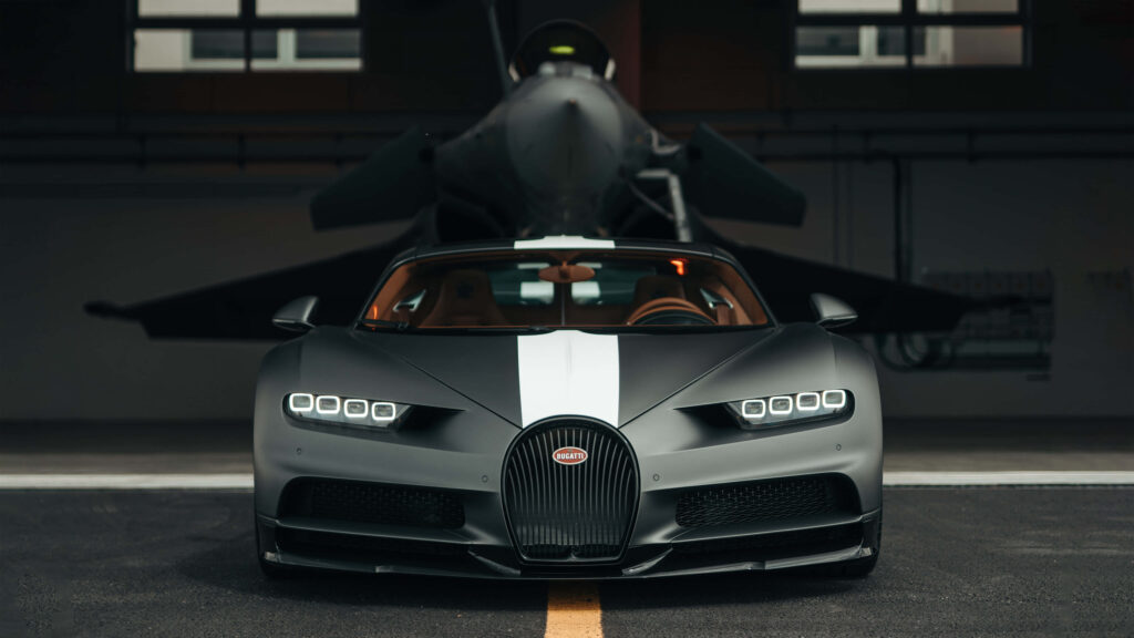 Matte black Bugatti Chiron with white stripe in front of fighter jet showcasing speed luxury engineering Wallpaper