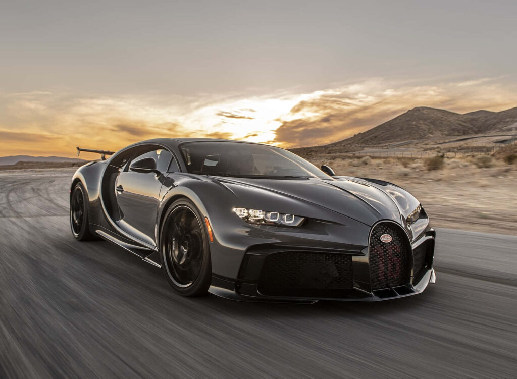 Black Bugatti Chiron speeding at sunset in desert showcasing luxury supercar design wallpaper