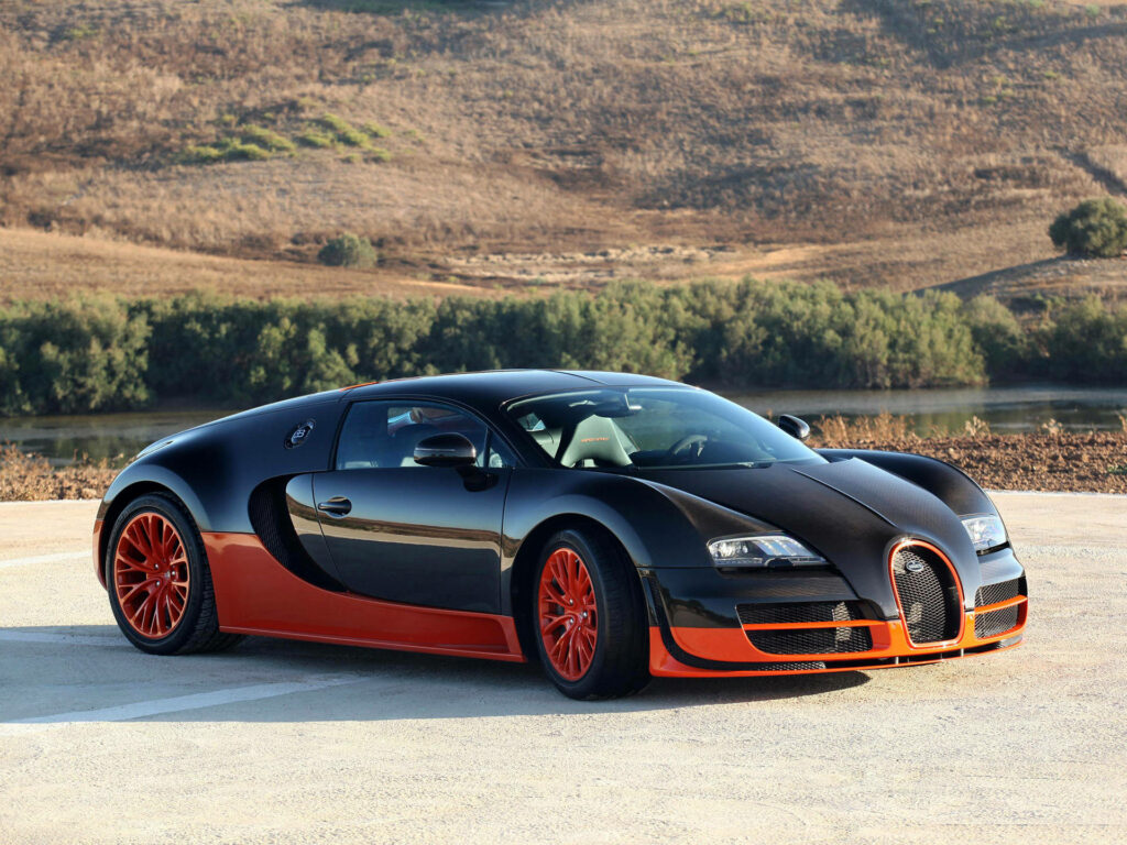 Bugatti Veyron black and orange two-tone with red wheels parked outdoors on sunny day wallpaper