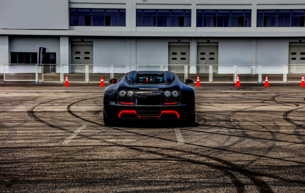 Rear view of red black Bugatti Veyron on tarmac with tire marks and orange cones wallpaper background