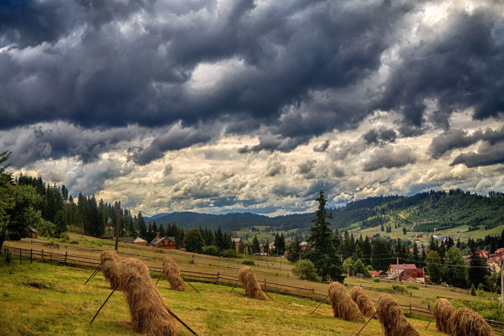 Bukovel Carpathians Ukraine peaceful field haystacks rustic houses pine forest dramatic sky wallpaper