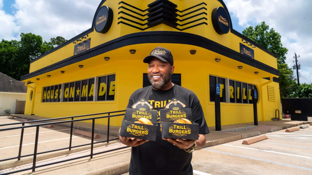 Bun B poses outside Trill Burgers in yellow black holding signature burger boxes urban street style Wallpaper