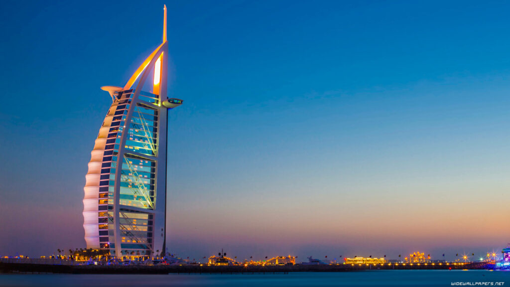 Burj Al Arab Dubai glowing at twilight with vibrant blue and gold hues over calm water wallpaper