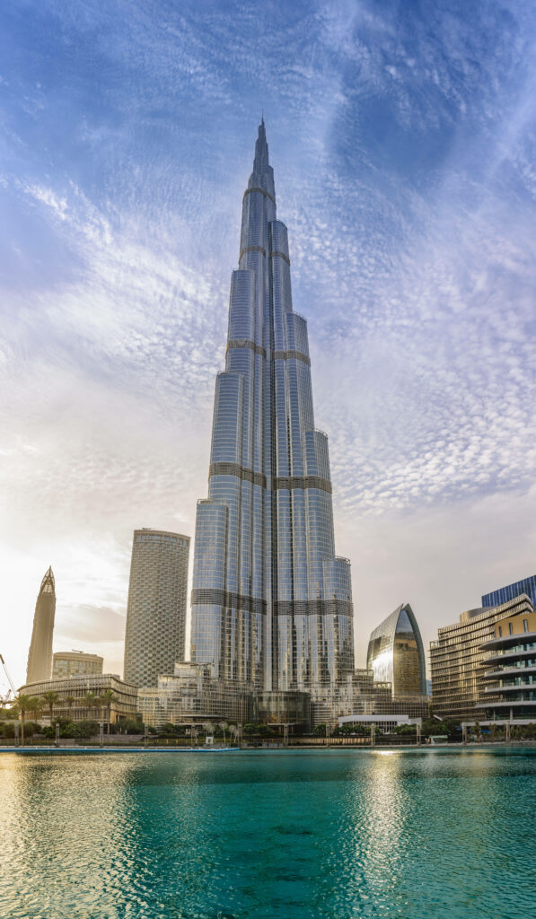 Burj Khalifa towering under cloudy sky with modern skyscrapers and turquoise water foreground Wallpaper