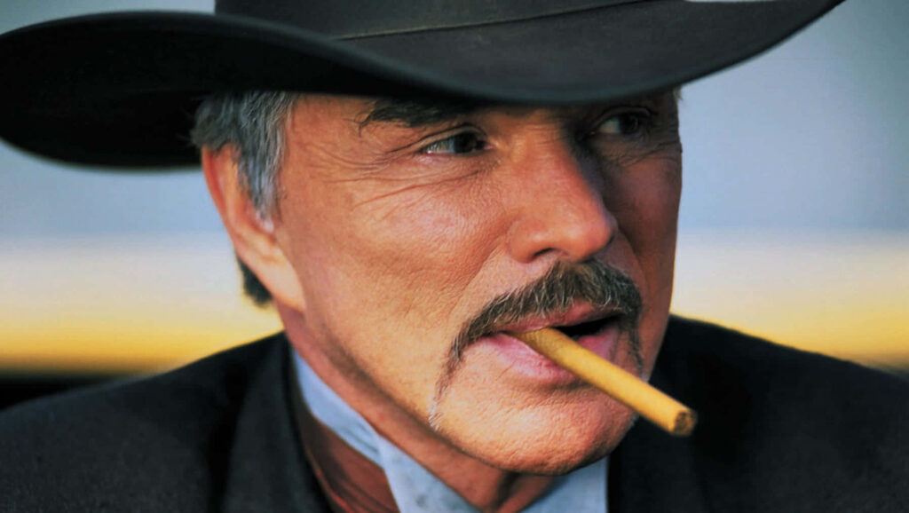 Burt Reynolds close-up portrait in cowboy hat with mustache and cigar vibrant red wallpaper