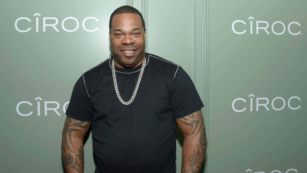 Busta Rhymes in black shirt and silver chain with tattoos at CIROC event green branded background Wallpaper