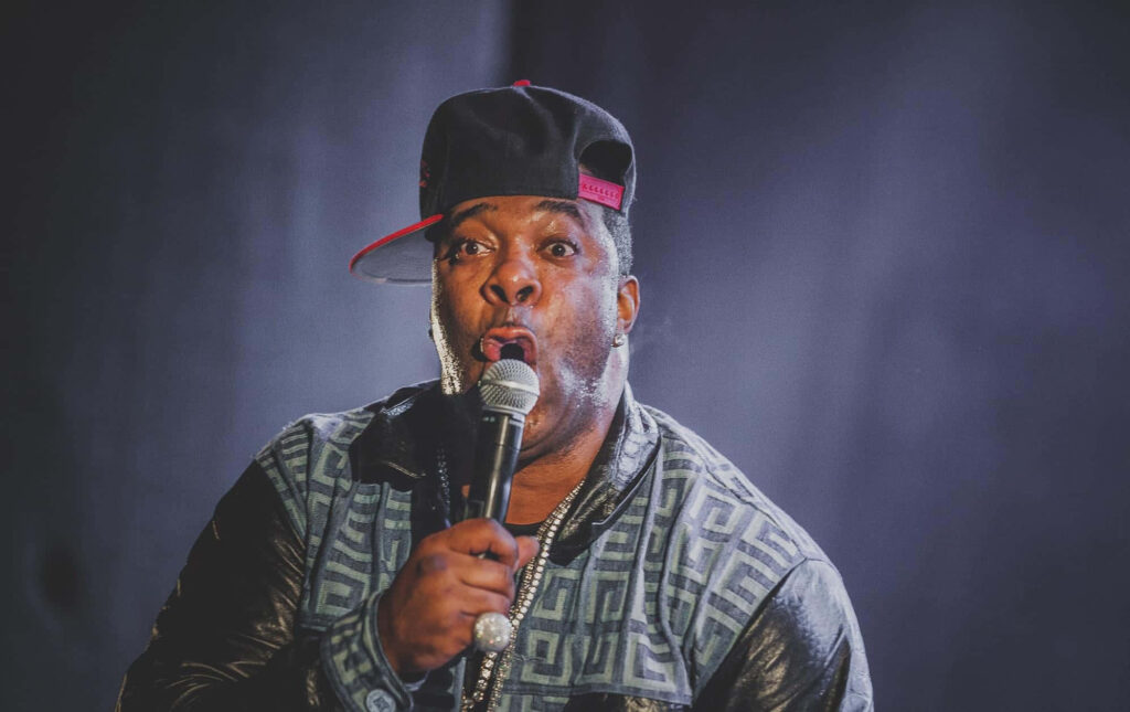 Busta Rhymes performing live in patterned jacket and tilted cap with vibrant stage lighting Wallpaper
