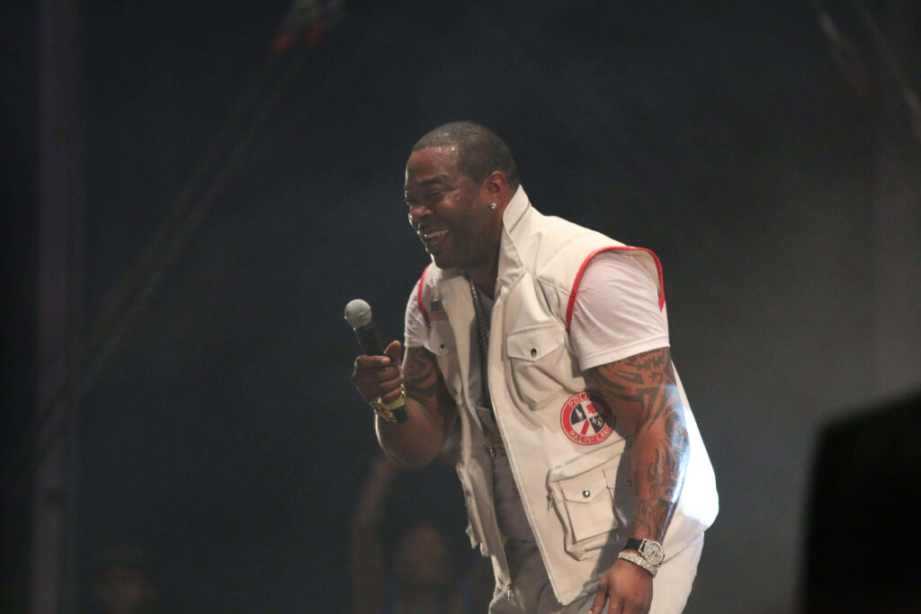 Busta Rhymes live concert vibrant smile energetic pose white vest red accents tattoos stage lighting Wallpaper