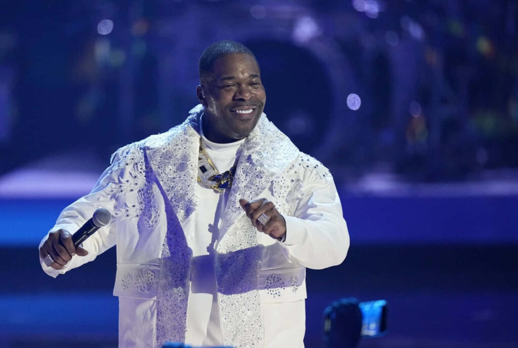 Busta Rhymes performing live in vibrant patterned white outfit with dynamic concert lighting Wallpaper