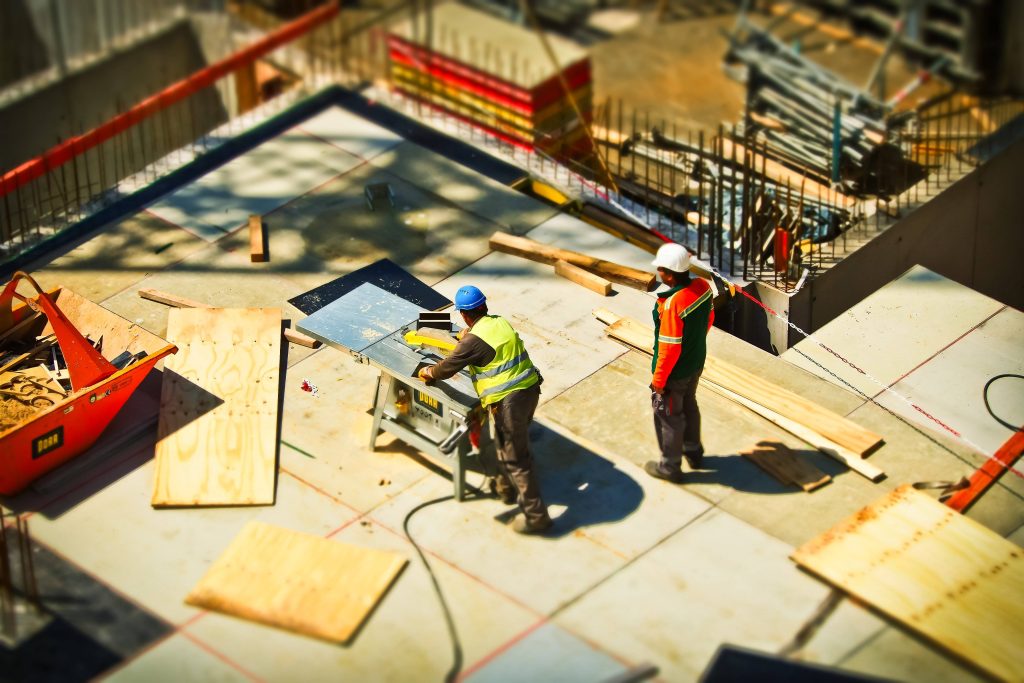 High-angle tilt-shift of construction workers cutting lumber on site with safety gear and tools Wallpaper