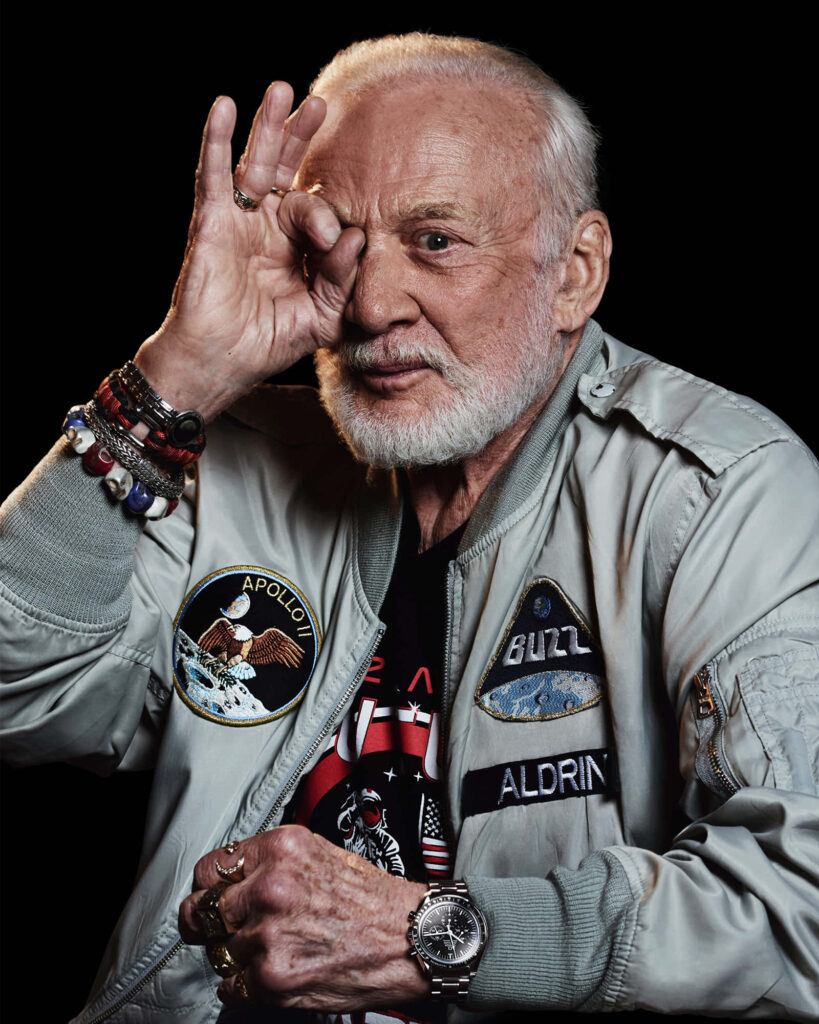 Buzz Aldrin portrait in silver Apollo jacket saluting with dark background and mission patches Wallpaper