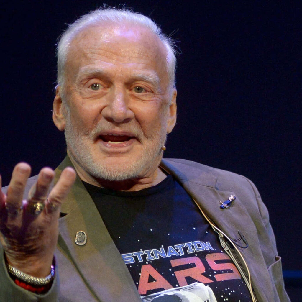 Buzz Aldrin speaking passionately wearing Destination Mars shirt against dark event background Wallpaper