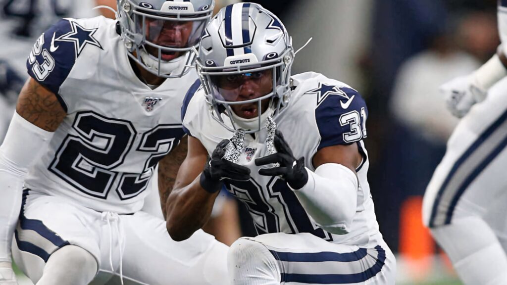 Byron Jones signals defensive play in Dallas Cowboys white silver uniforms on vibrant football field Wallpaper
