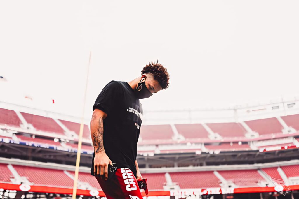 Byron Murphy focused on field in black shirt and mask with vibrant red stadium seats background Wallpaper
