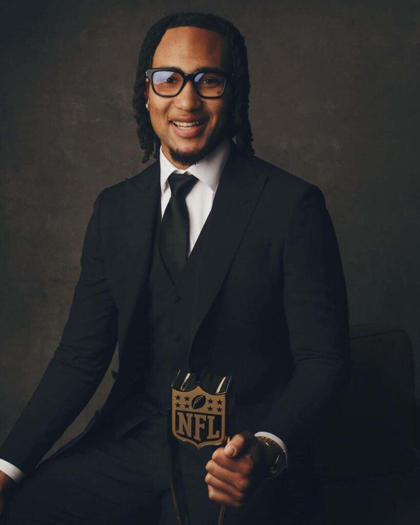 C J Stroud in black suit holding golden NFL trophy confident portrait dark background wallpaper