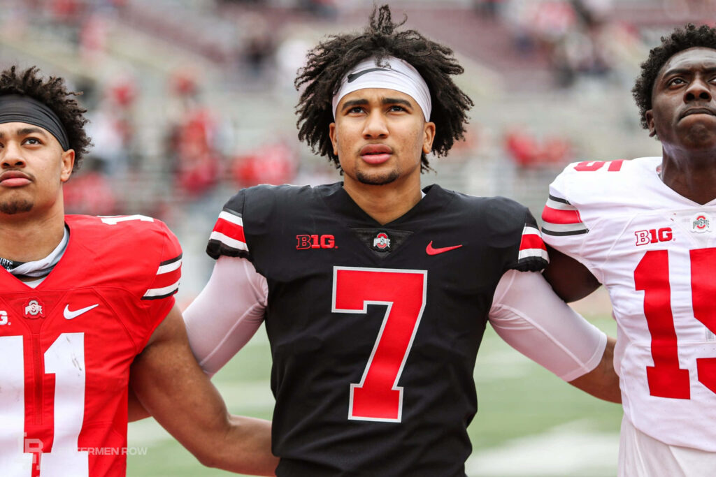 C J Stroud in Ohio State uniform leads teammates on field showcasing college football unity and spirit Wallpaper