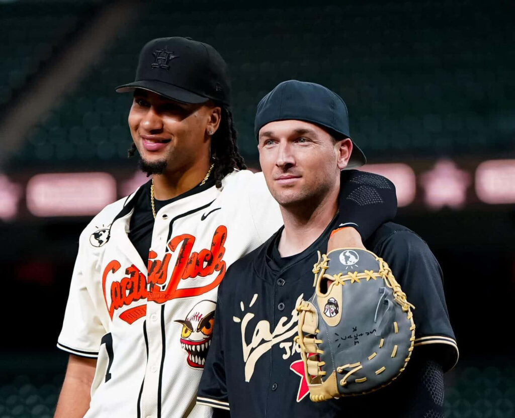 C J Stroud on baseball field in white jersey smiling with teammate in black stadium background Wallpaper