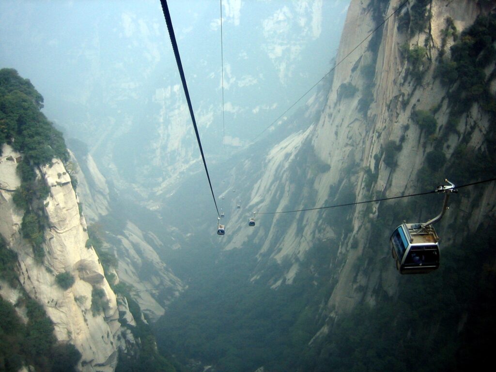 Cable lift cabins suspended above a misty deep gorge with steep green rocky cliffs landscape Wallpaper
