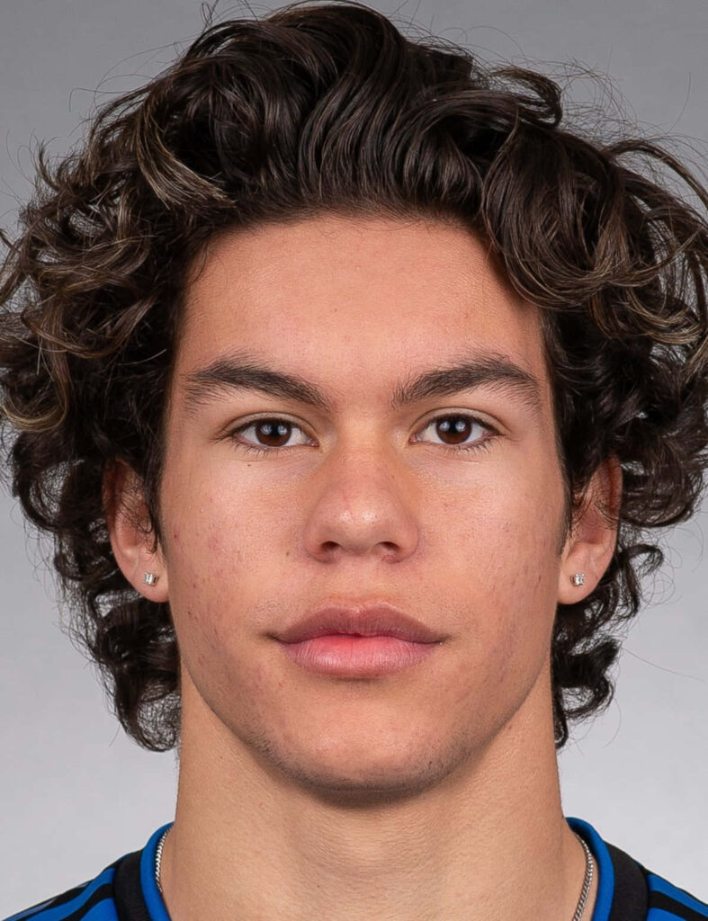 Close-up portrait of Cade Cowell with curly hair in blue black jersey on gray background wallpaper
