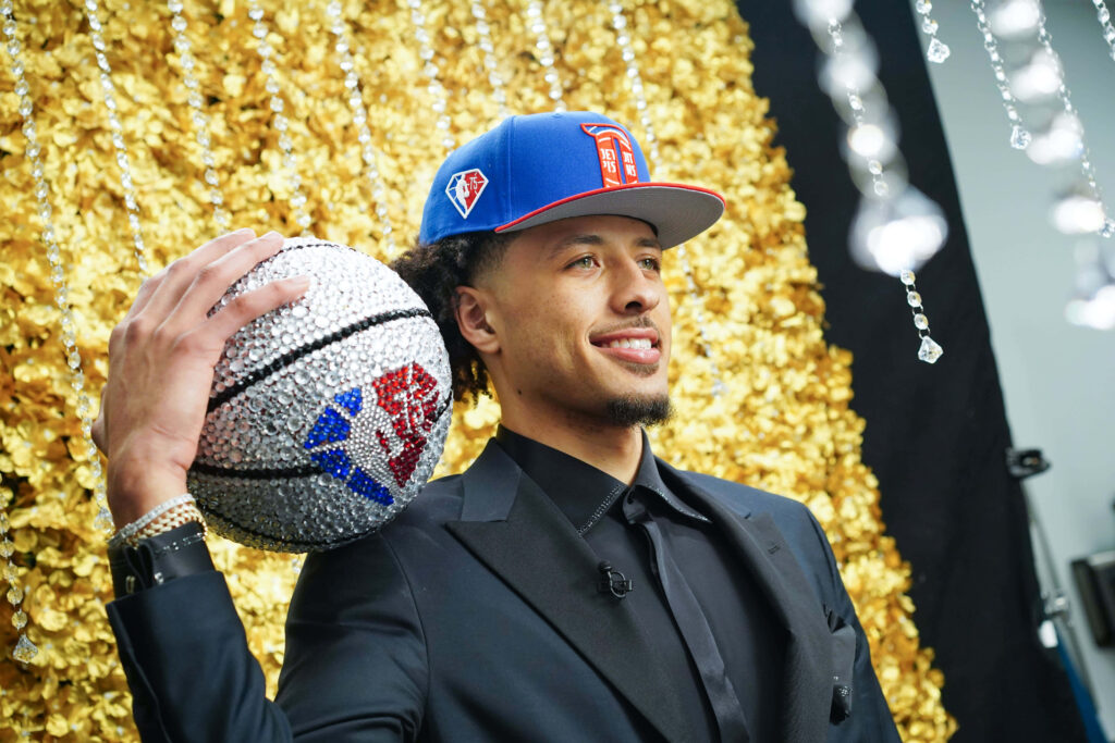 Cade Cunningham in black suit holding rhinestone basketball with golden floral NBA Draft background Wallpaper