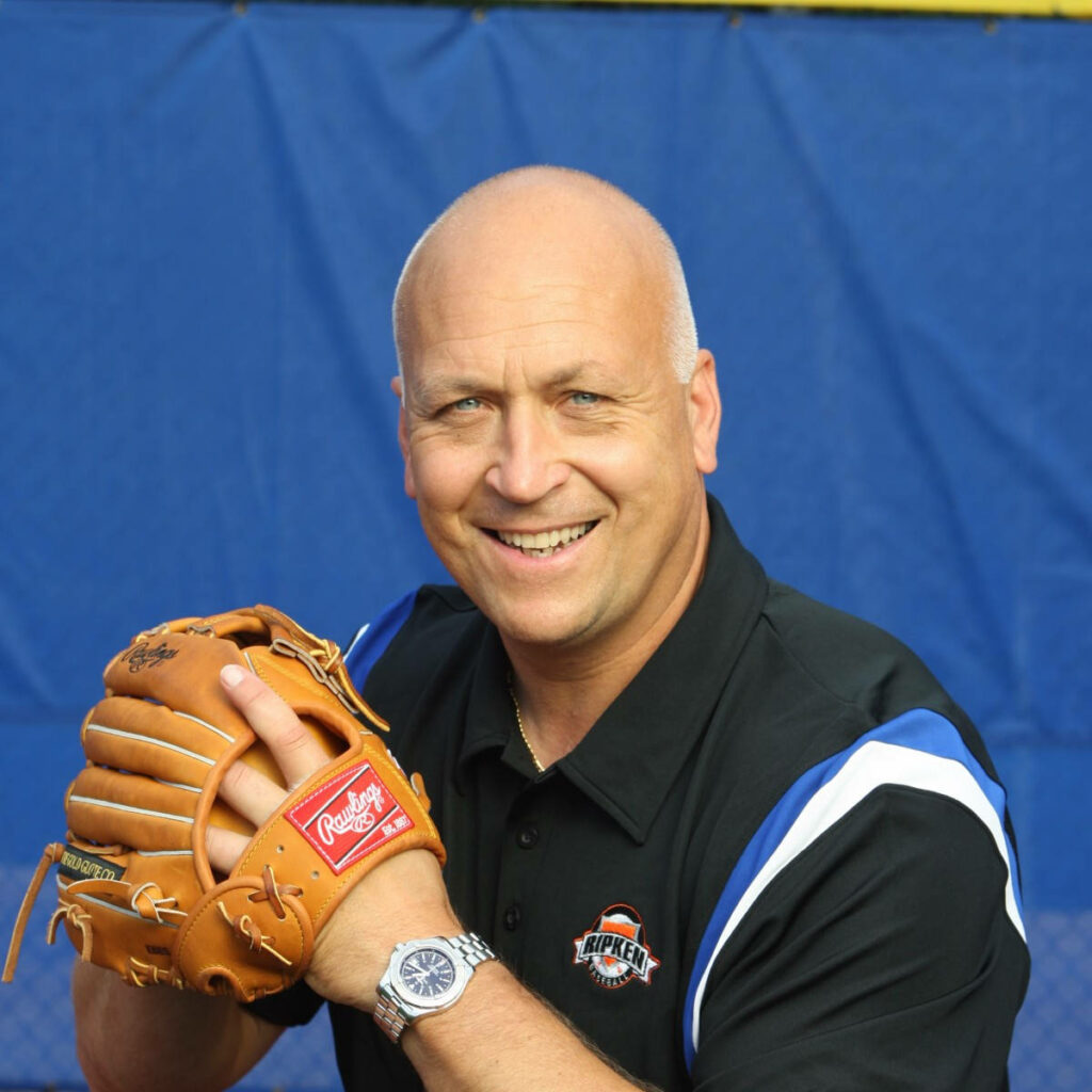 Cal Ripken Jr smiling with Rawlings glove in Ripken Baseball polo vibrant blue yellow background Wallpaper